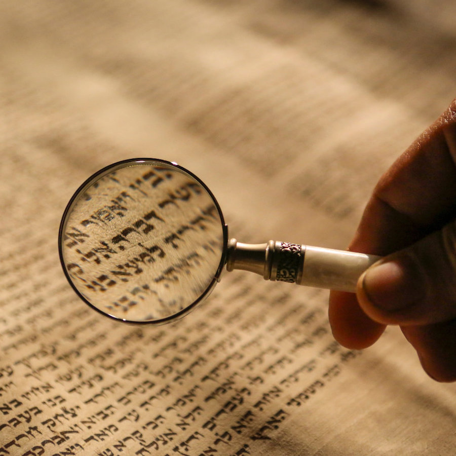 Hand holding magnifying glass over a torah scroll